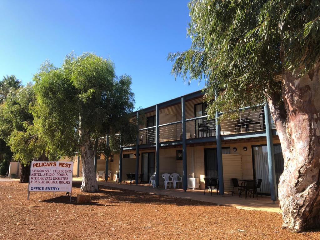 Exterior view of Pelican’s Nest in Kalbarri, showing shaded veranda, tall trees, and signage for self-catering units and motel rooms