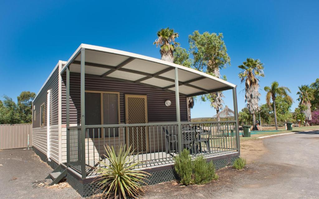 Self-contained holiday cabin at a caravan park in Kalbarri, Western Australia, with outdoor seating and palm trees in the background.
