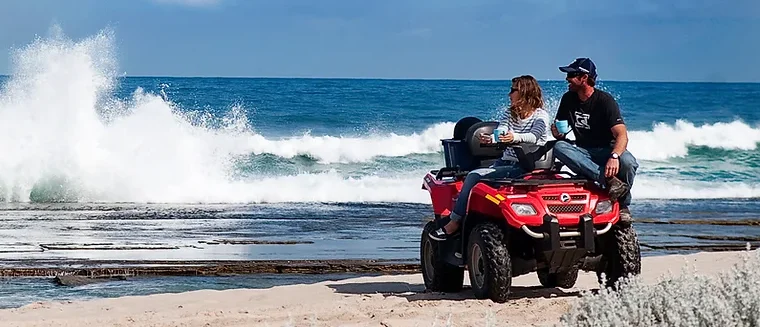 A couple on a quad bike enjoying the view of powerful ocean waves crashing against the shore at Wagoe Beach Quad Biketours, Kalbarri.