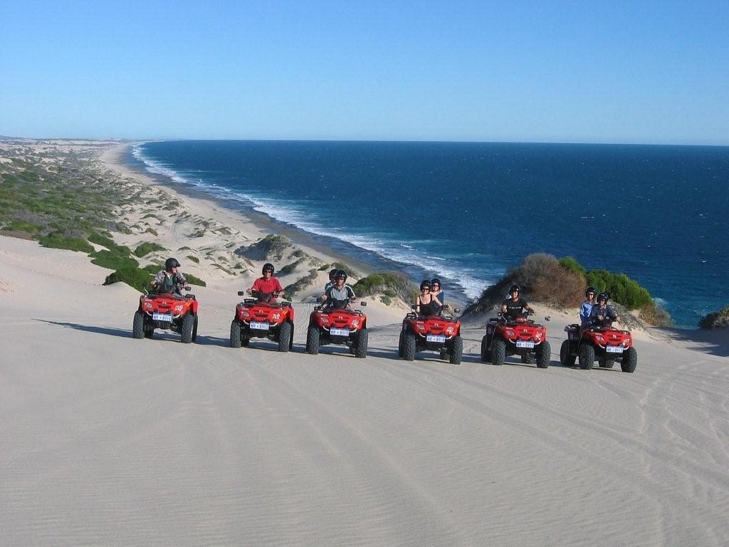 A group of quadbike riders lined up on a sand dune with sweeping views of Wagoe Beach and the deep blue Indian Ocean in Kalbarri, Western Australia.