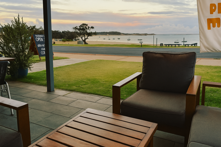 Outdoor café seating with armchairs overlooking the Murchison River in Kalbarri, Western Australia, on a calm overcast day. Boats float peacefully in the bay under a soft sky.