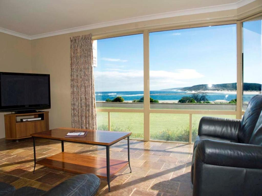 Oceanfront lounge room at Pelican Shore Villa 6 with leather seating, flat-screen TV, and panoramic views of the river and ocean through large glass windows.